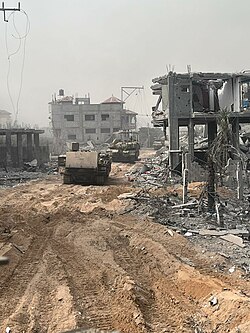 Zwei Panzer rollen auf Schmutz, umgeben von einer massiven Zerstörung. Es gibt Trümmer auf dem Boden, und Gebäude, die explodiert wurden