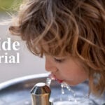 Kind trinkt aus Wasserbrunnen mit Text, der besagt, dass Fluorid vor Gericht steht