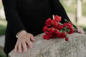 person standing in front of a gravestone with red flowers